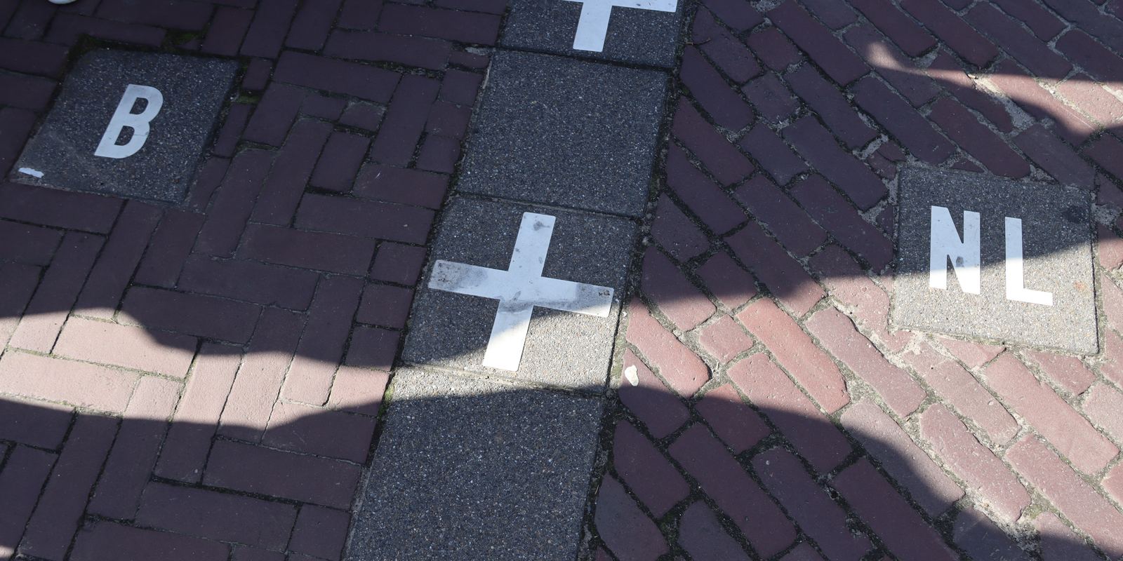 A border line of white crosses on the pavement in Baarle with B and NL on either side