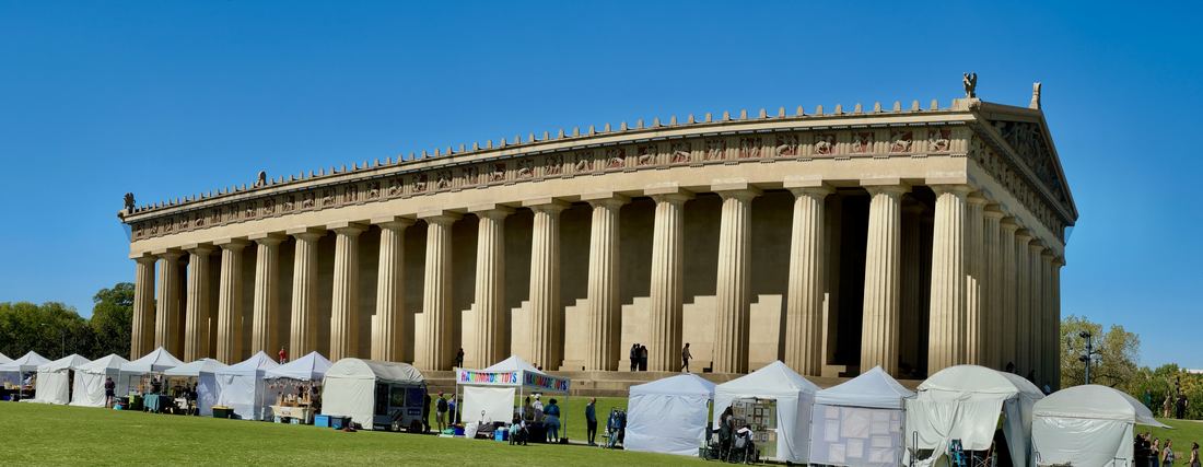 Wide view of the full-scale Parthenon replica with its rows of columns in Centennial Park, Nashville, with craft fair tents in front