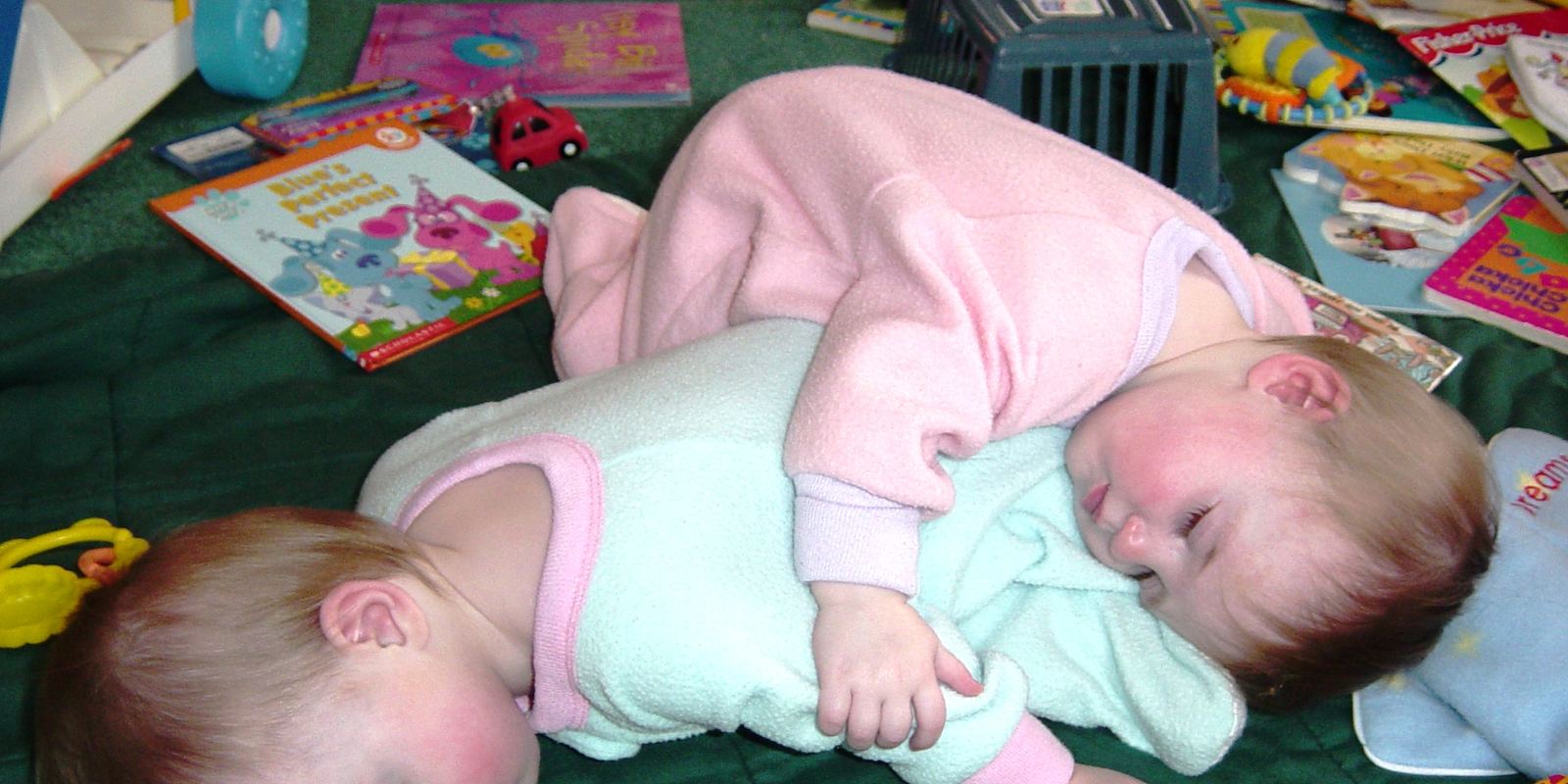 Two baby twin sisters lying together, one resting on the other